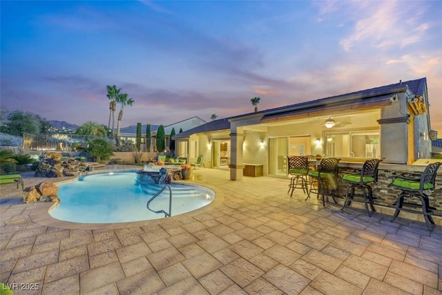 pool at dusk featuring a patio and an outdoor bar