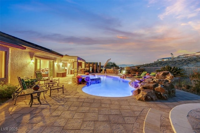 pool at dusk with a patio and pool water feature