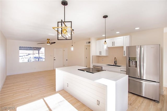 kitchen featuring a center island, sink, stainless steel fridge, decorative light fixtures, and white cabinets