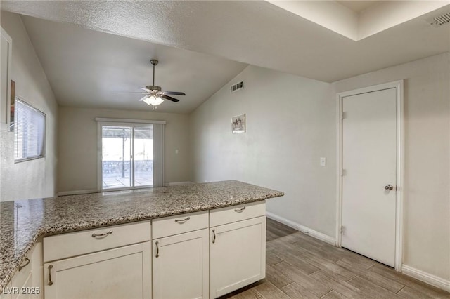 kitchen with ceiling fan, light stone counters, kitchen peninsula, lofted ceiling, and white cabinets