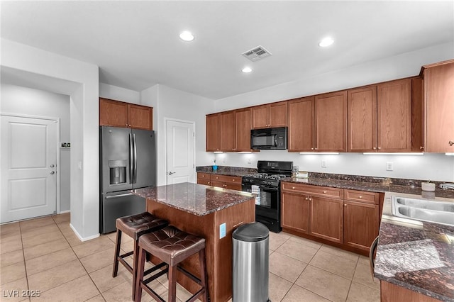 kitchen with a kitchen bar, sink, black appliances, light tile patterned floors, and a kitchen island