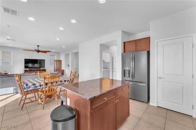 kitchen with a center island, ceiling fan, stainless steel fridge, dark stone countertops, and light tile patterned flooring