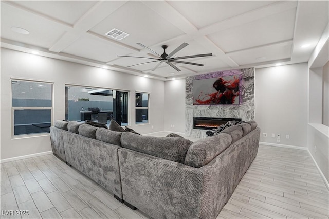 living room with ceiling fan, coffered ceiling, and a stone fireplace