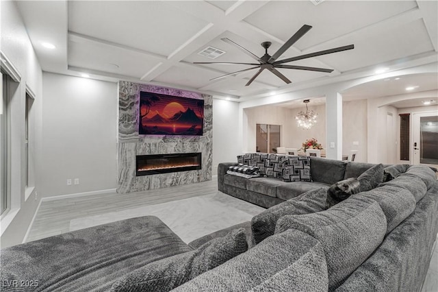 living room featuring coffered ceiling, a premium fireplace, and ceiling fan with notable chandelier