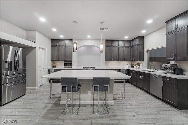 kitchen with sink, a center island, dark brown cabinets, pendant lighting, and appliances with stainless steel finishes