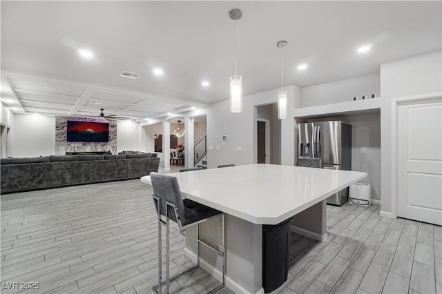 kitchen with a kitchen bar, ceiling fan, hanging light fixtures, stainless steel refrigerator with ice dispenser, and a kitchen island