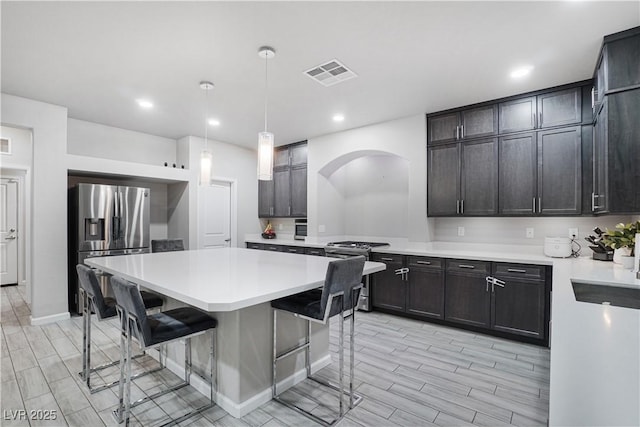 kitchen with decorative light fixtures, a center island, a breakfast bar area, dark brown cabinetry, and appliances with stainless steel finishes