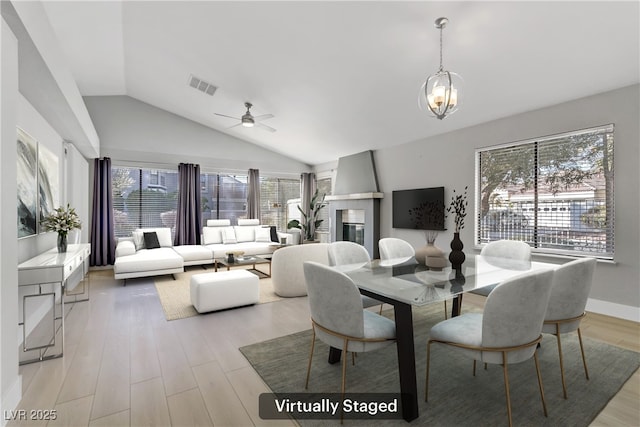 dining area featuring ceiling fan with notable chandelier, light hardwood / wood-style floors, a wealth of natural light, and vaulted ceiling