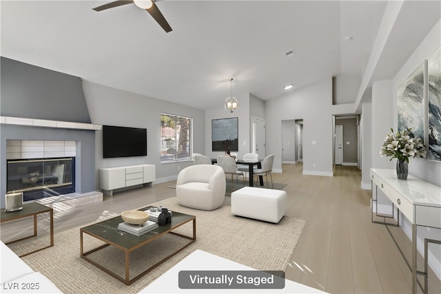 living room with a fireplace, ceiling fan with notable chandelier, light hardwood / wood-style flooring, and vaulted ceiling