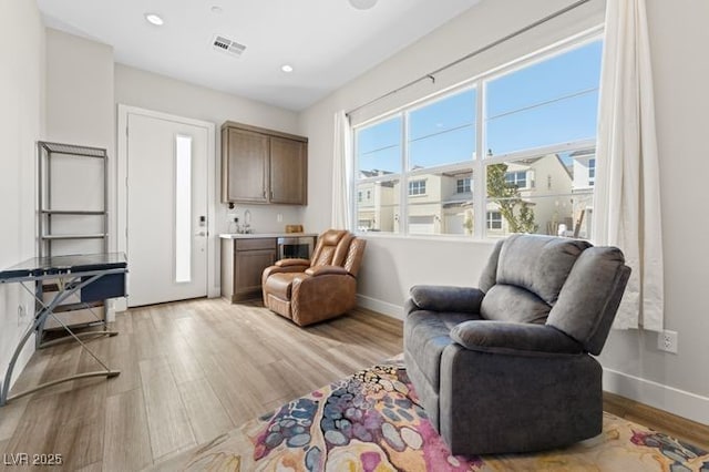 living area with light wood-style flooring, visible vents, and baseboards