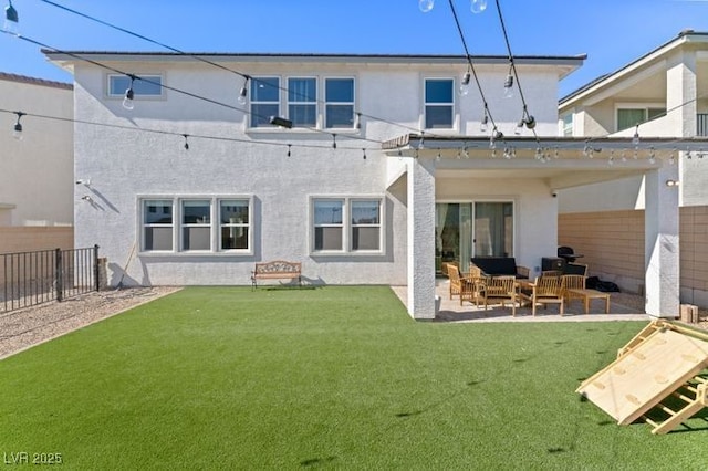 rear view of property featuring a lawn, fence, and stucco siding