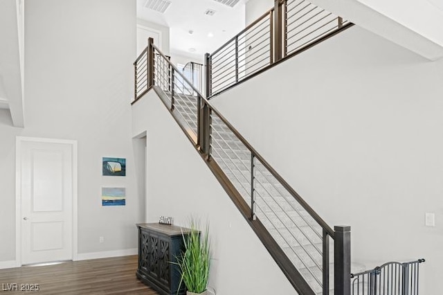 stairs with visible vents, a towering ceiling, baseboards, and wood finished floors