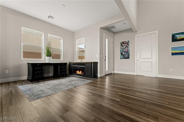 bar featuring a warm lit fireplace, dark wood-type flooring, visible vents, and baseboards