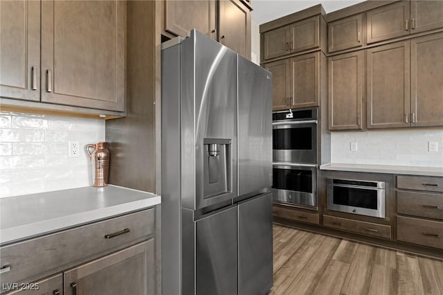 kitchen featuring stainless steel appliances, light wood-type flooring, light countertops, and decorative backsplash