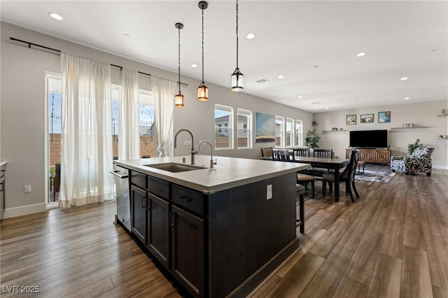 kitchen featuring a center island with sink, light countertops, hanging light fixtures, open floor plan, and a sink