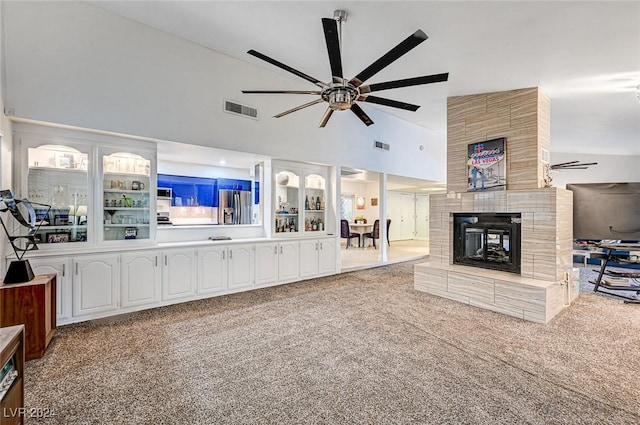 living room featuring a tiled fireplace, light carpet, ceiling fan, and high vaulted ceiling