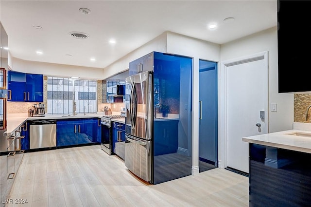 kitchen with appliances with stainless steel finishes, light wood-type flooring, backsplash, blue cabinets, and sink