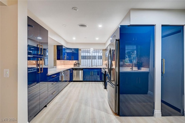 kitchen with backsplash, sink, light hardwood / wood-style flooring, blue cabinetry, and stainless steel appliances