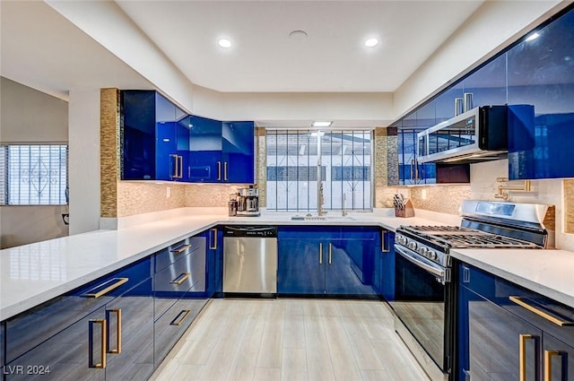 kitchen with appliances with stainless steel finishes, backsplash, sink, blue cabinetry, and light hardwood / wood-style floors