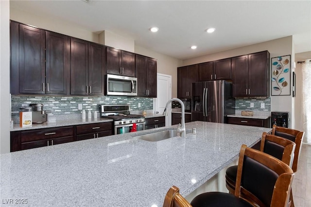 kitchen with decorative backsplash, light stone counters, dark brown cabinets, stainless steel appliances, and sink