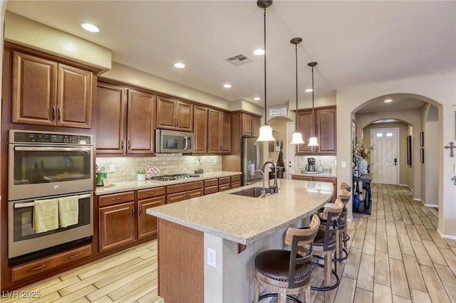 kitchen featuring light stone countertops, appliances with stainless steel finishes, sink, hanging light fixtures, and an island with sink