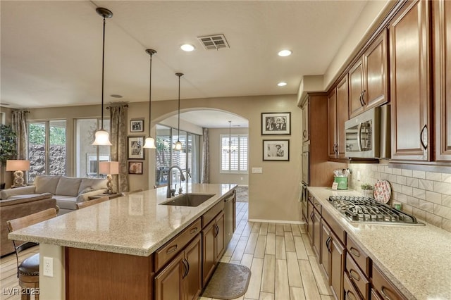 kitchen with backsplash, sink, an island with sink, appliances with stainless steel finishes, and light stone counters