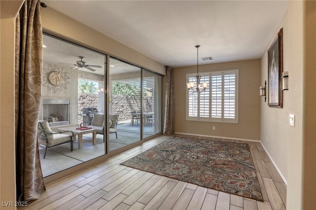 doorway to outside with a stone fireplace, a healthy amount of sunlight, light hardwood / wood-style floors, and ceiling fan with notable chandelier