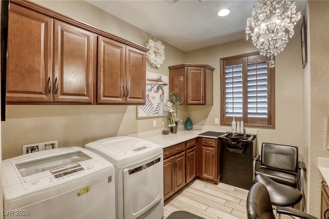 clothes washing area featuring washer and clothes dryer, a notable chandelier, and cabinets