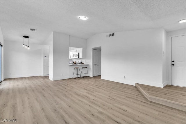 unfurnished living room featuring light hardwood / wood-style floors, lofted ceiling, and a textured ceiling