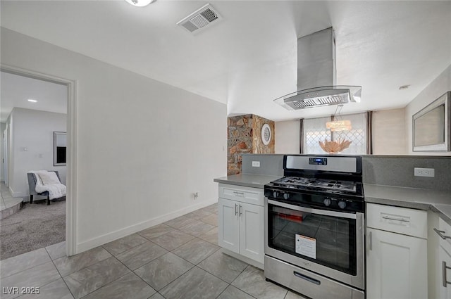 kitchen with light colored carpet, exhaust hood, white cabinetry, hanging light fixtures, and stainless steel range with gas stovetop