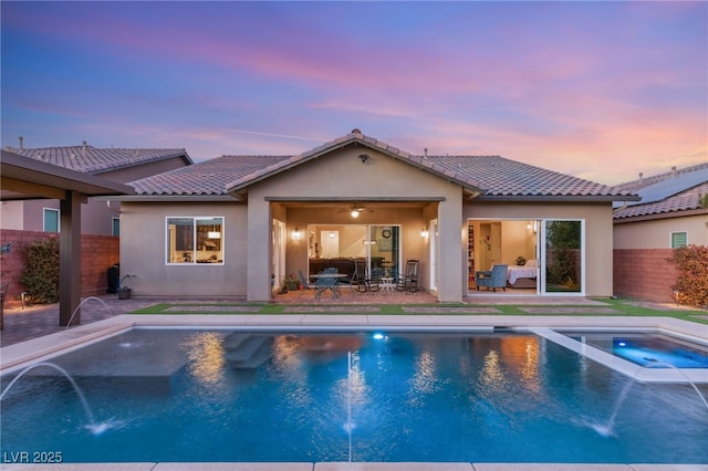 pool at dusk featuring an in ground hot tub, pool water feature, and a patio area