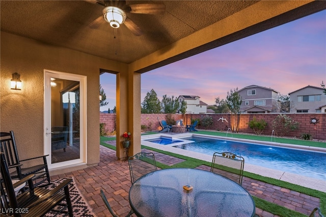 pool at dusk with an in ground hot tub, pool water feature, ceiling fan, and a patio area