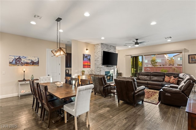 dining space featuring a stone fireplace, dark wood-type flooring, and ceiling fan