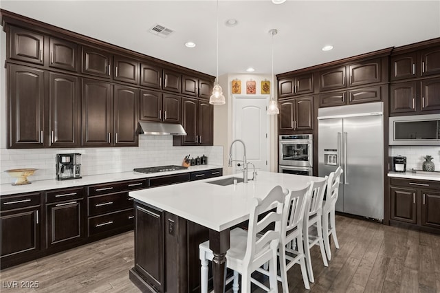 kitchen featuring hanging light fixtures, sink, built in appliances, and dark brown cabinetry