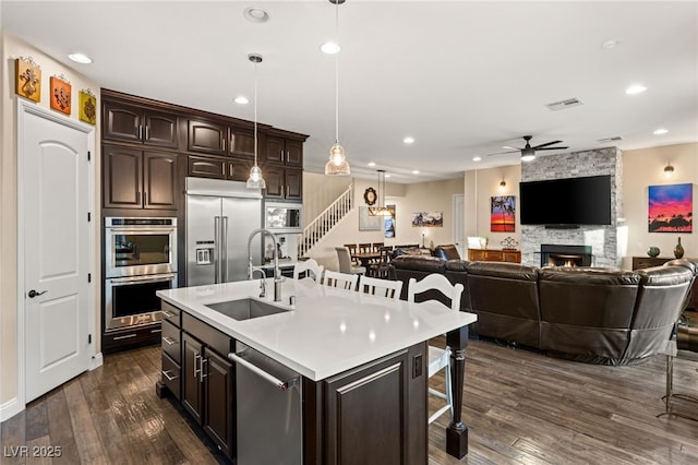 kitchen featuring an island with sink, appliances with stainless steel finishes, dark brown cabinets, and pendant lighting