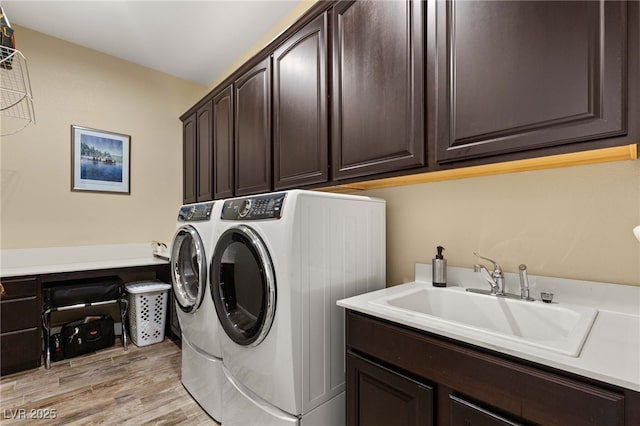 clothes washing area featuring light hardwood / wood-style flooring, sink, washer and clothes dryer, and cabinets