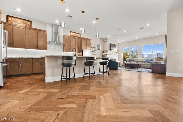 kitchen featuring light stone countertops, a kitchen breakfast bar, parquet floors, wall chimney range hood, and a large island