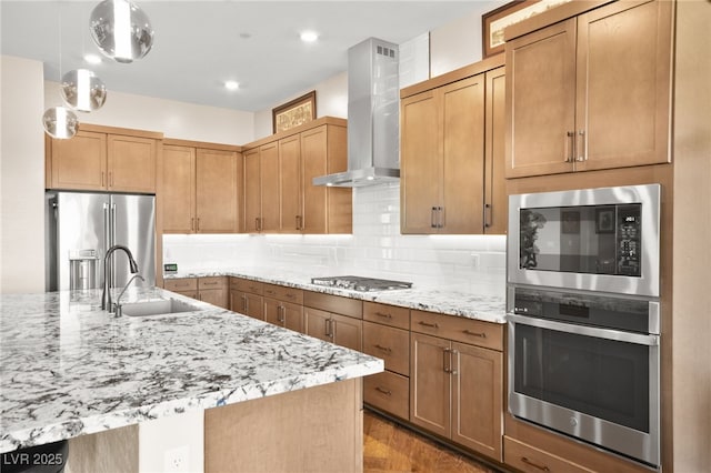 kitchen with sink, wall chimney exhaust hood, stainless steel appliances, backsplash, and decorative light fixtures