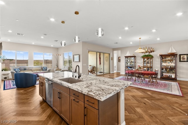 kitchen featuring light stone countertops, parquet floors, sink, pendant lighting, and an island with sink