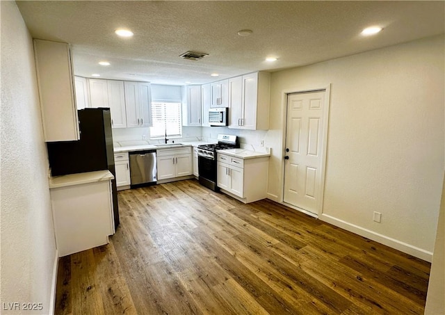 kitchen with wood-type flooring, white cabinetry, sink, and appliances with stainless steel finishes