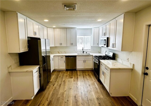 kitchen featuring black appliances, white cabinets, sink, light hardwood / wood-style flooring, and a textured ceiling