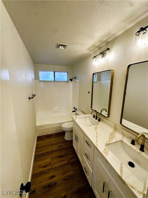 full bathroom featuring bathing tub / shower combination, hardwood / wood-style floors, a textured ceiling, toilet, and vanity