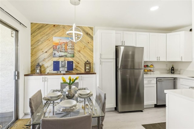 kitchen with pendant lighting, wood walls, white cabinetry, and appliances with stainless steel finishes