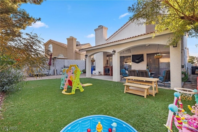 back of property featuring a patio, an outdoor hangout area, a playground, and a lawn