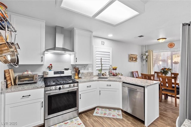 kitchen featuring white cabinetry, wall chimney exhaust hood, kitchen peninsula, light hardwood / wood-style flooring, and appliances with stainless steel finishes