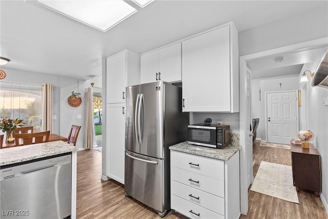 kitchen featuring light stone counters, white cabinets, appliances with stainless steel finishes, and light hardwood / wood-style floors