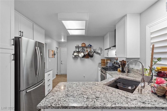 kitchen with sink, white cabinets, kitchen peninsula, light stone countertops, and appliances with stainless steel finishes