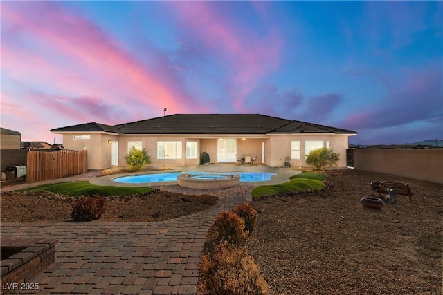 back house at dusk featuring a patio area and a pool with hot tub