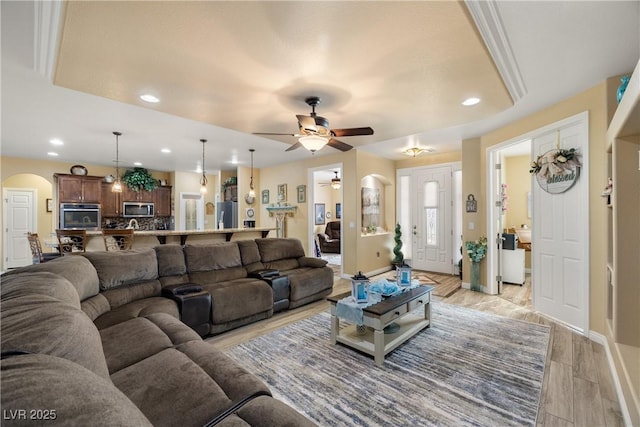 living room with a raised ceiling, ceiling fan, and light wood-type flooring