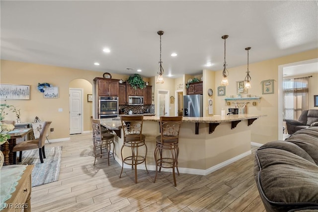 kitchen with light stone countertops, hanging light fixtures, stainless steel appliances, a kitchen bar, and decorative backsplash